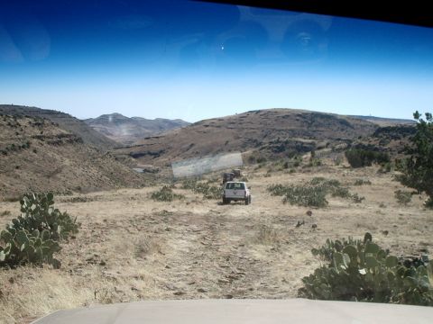 1996 Ford Bronco - A convoy of SUVs navigates a dusty trail through a barren, arid landscape under a clear blue sky.