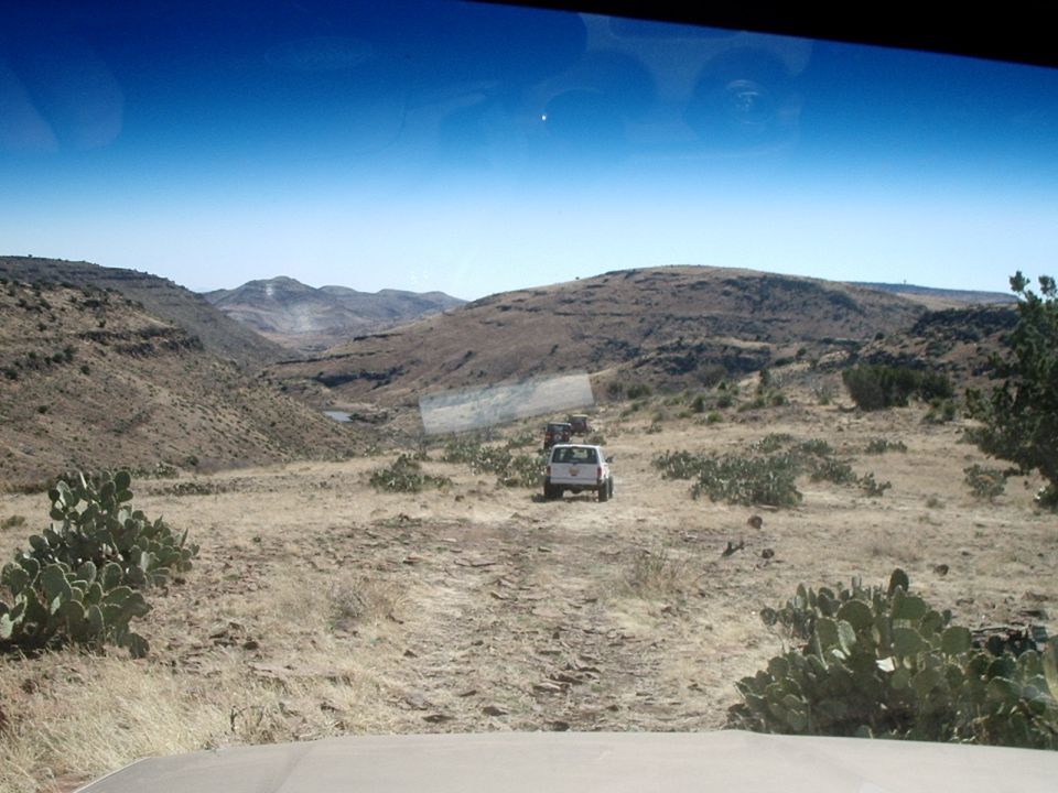 Two SUVs driving on a dirt road through a dry, hilly area with cacti
