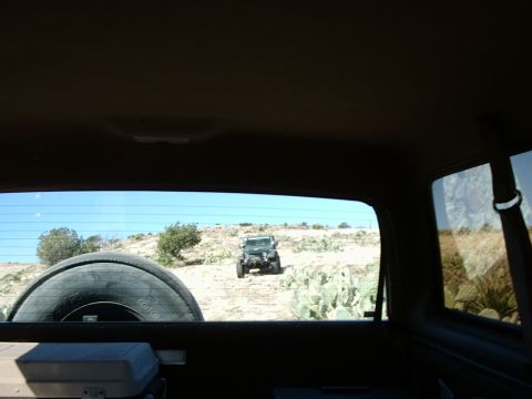 1996 Ford Bronco - A Jeep Wrangler navigates a dry, desert-like trail, viewed from inside another vehicle.