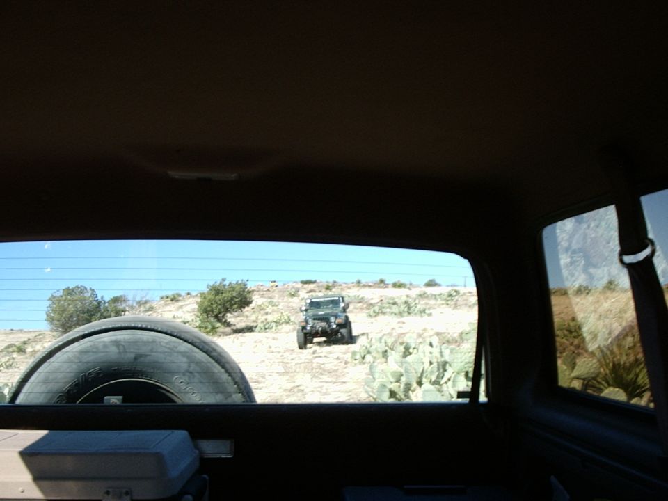 Jeep Wrangler driving on a dusty trail with cacti and sparse vegetation