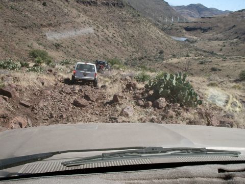 1996 Ford Bronco - Two off-road vehicles navigate a steep, rocky mountain path under a clear sky.