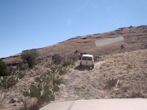 1996 Ford Bronco - Two SUVs navigate a rough, uphill dirt path through a dry, arid landscape under a clear blue sky.