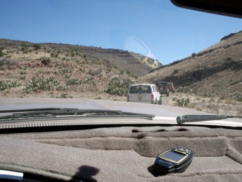 1996 Ford Bronco - Several SUVs travel in a convoy on a dusty trail through a dry, hilly landscape under a clear blue sky.