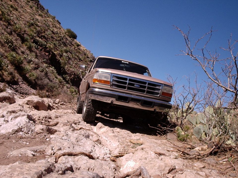 Tan 1992 Ford Bronco driving on a rocky, arid trail