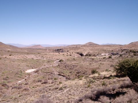 1996 Ford Bronco - A wide view of a dry, arid landscape with sparse vegetation and a winding dry creek bed, under a bright blue sky.