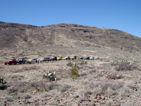 1996 Ford Bronco - A convoy of SUVs and trucks are stopped on a dusty trail with a large hill in the background.