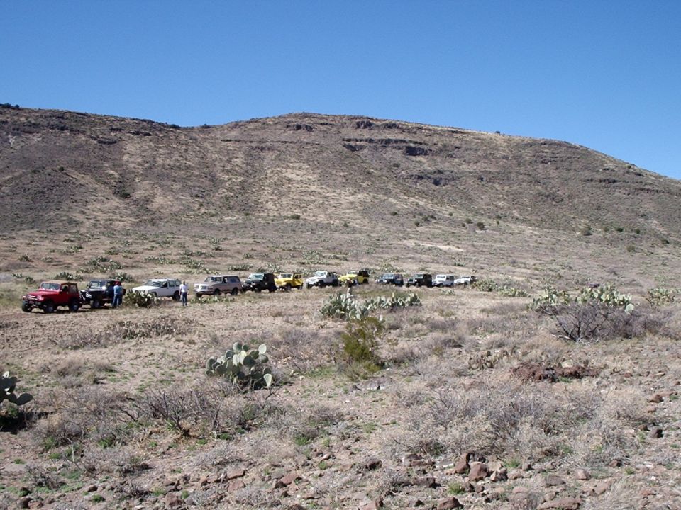 Line of off-road vehicles parked on a dirt trail in a desert landscape