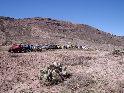 1996 Ford Bronco - A convoy of off-road vehicles is parked on a dusty trail under a clear blue sky.