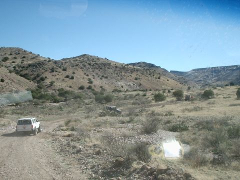 1996 Ford Bronco - Several vehicles traverse a dusty trail through a barren, arid landscape under a clear blue sky.