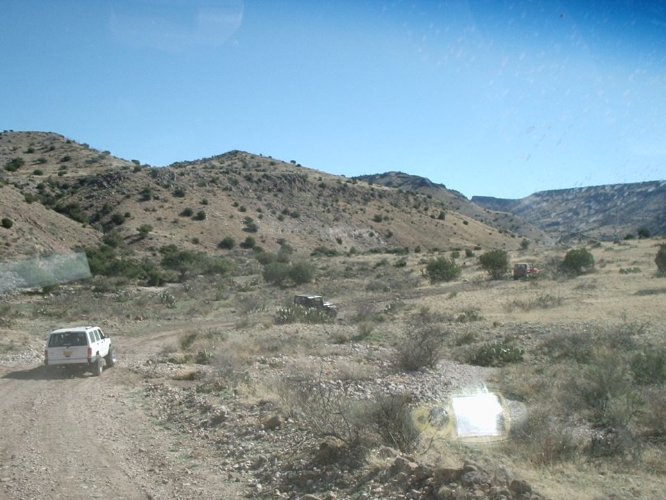 White SUV and two other vehicles on a dirt road in a dry, hilly area