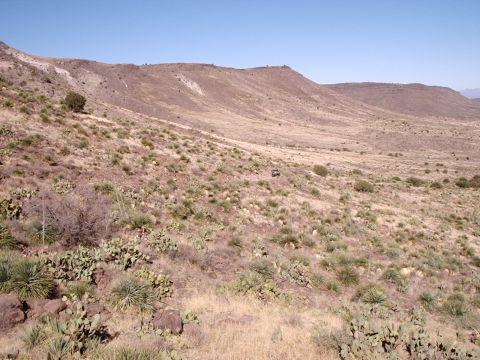 1996 Ford Bronco - A lone SUV traverses a desolate, arid landscape with sparse vegetation and rolling hills.