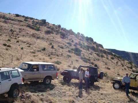1996 Ford Bronco - Several off-road vehicles are parked on a hillside under a bright sun.