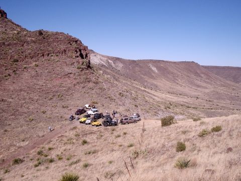 1996 Ford Bronco - Several SUVs, including a 1996 Ford Bronco, are gathered on a dusty trail in a vast, arid canyon under a clear blue sky.