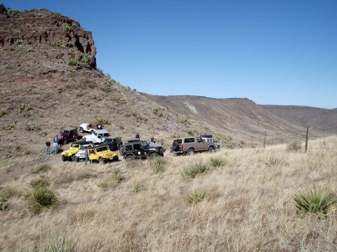 1996 Ford Bronco - A convoy of off-road vehicles, including a 1996 Ford Bronco, gathered on a dry, grassy slope under a clear blue sky.