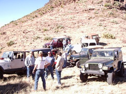 1996 Ford Bronco - A group of off-road vehicles and people gathered on a dry, hilly terrain under a clear blue sky.