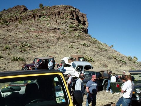 1996 Ford Bronco - Off-road vehicles and people gathered on a dry, hilly landscape under a clear blue sky.