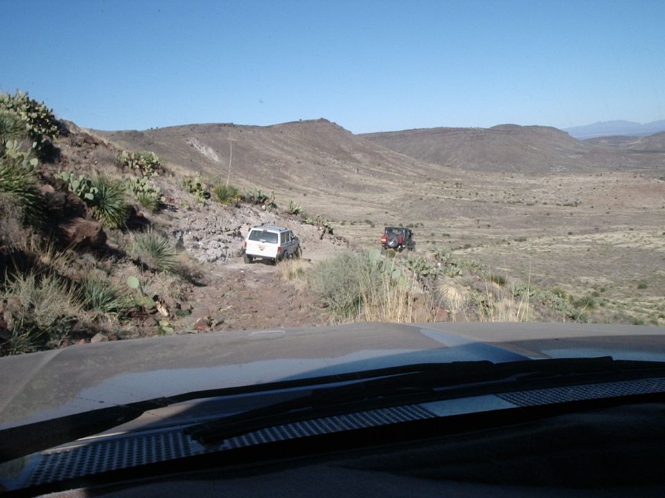 Two SUVs driving on a rocky dirt road in a desert landscape