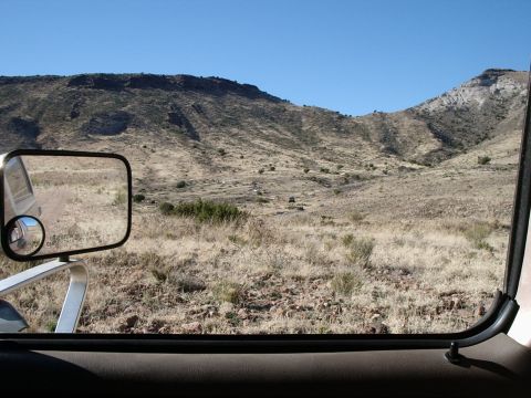 1996 Ford Bronco - View of a dry, hilly landscape from inside a vehicle, with a side mirror visible.