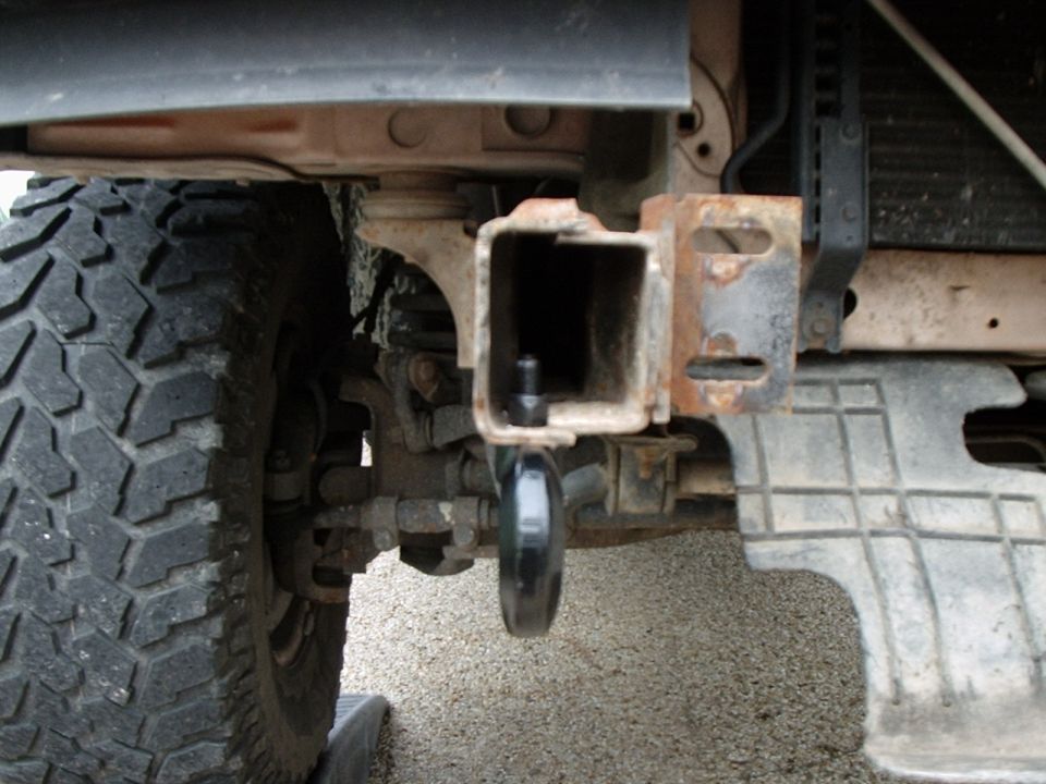 Close-up of rusted square receiver hitch and bracket under a truck bumper