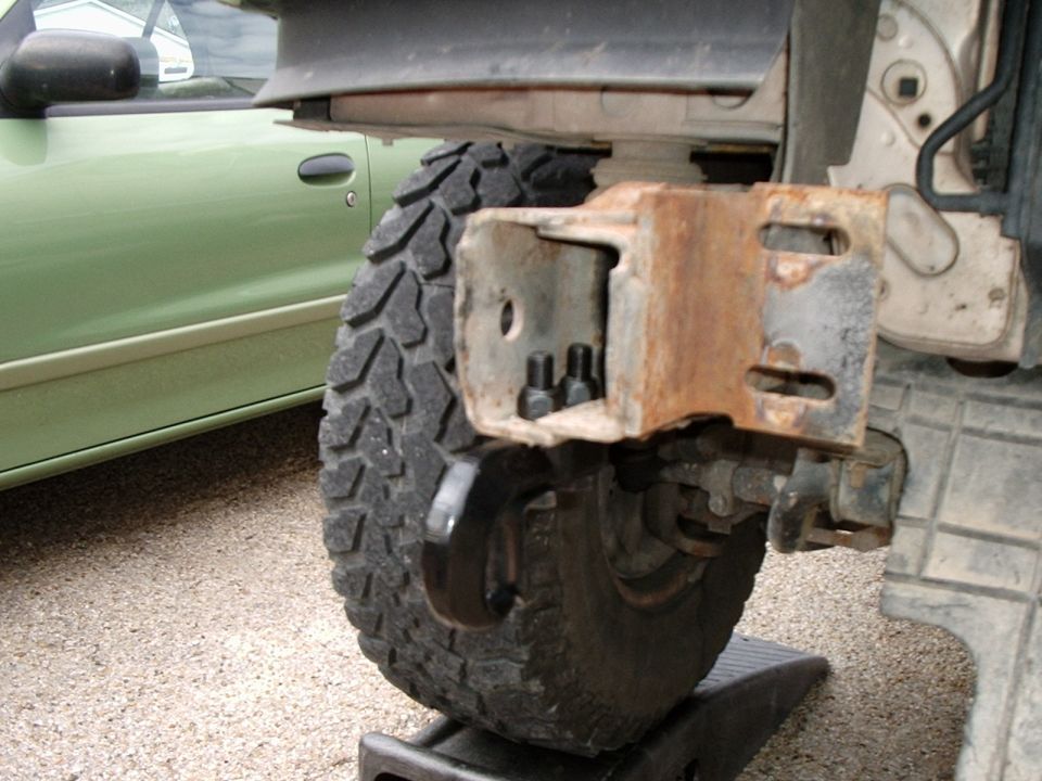 Rusty receiver hitch bracket under truck frame with mud tire on a wheel ramp