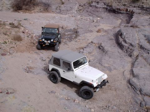 1996 Ford Bronco - Two Jeep Wranglers navigate a challenging off-road trail with rocky inclines and sandy patches.