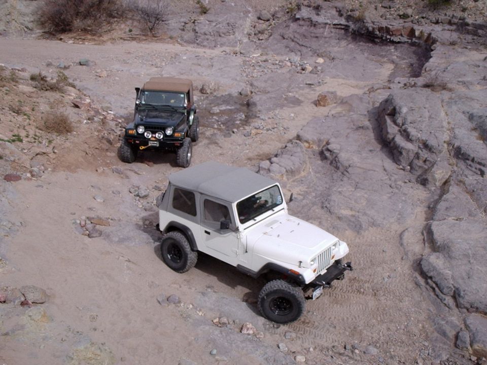 White Jeep Wrangler in foreground, black Jeep Wrangler behind on rocky terrain