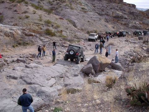 1996 Ford Bronco - Several off-road vehicles are seen on a challenging rocky trail in a desert landscape.