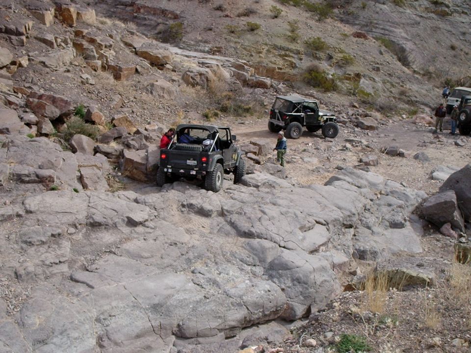 Black Jeep Wrangler off-roading on rocky terrain with other vehicles nearby