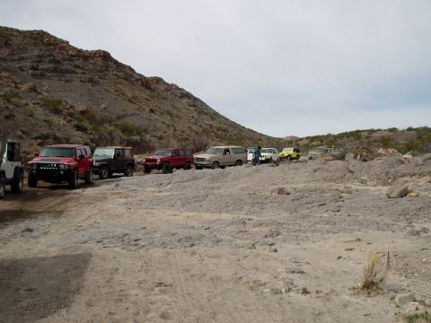 1996 Ford Bronco - A line of SUVs and off-road vehicles navigate a rocky trail in a desert landscape.