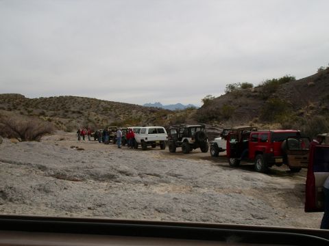 1996 Ford Bronco - A group of off-road vehicles are lined up on a rocky trail in a desert environment.