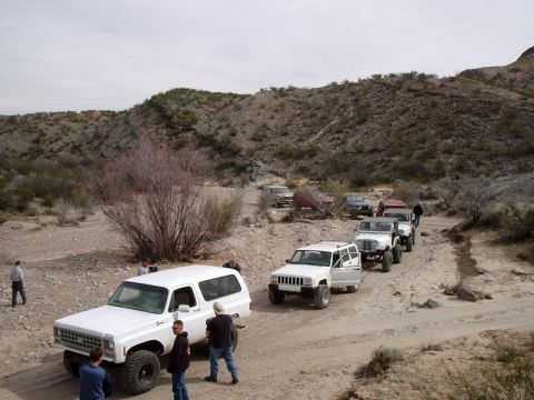1996 Ford Bronco - A group of off-road vehicles travels down a dusty trail through a barren, hilly landscape.