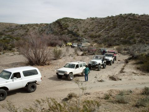 1996 Ford Bronco - A convoy of off-road vehicles navigates a dusty trail through a barren, hilly terrain.