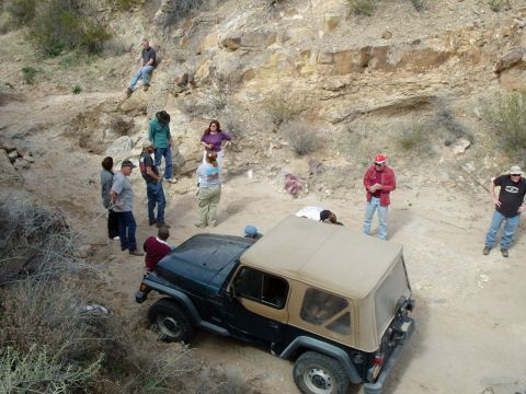 1996 Ford Bronco - Group of people observe a Jeep Wrangler TJ on a dusty off-road trail.
