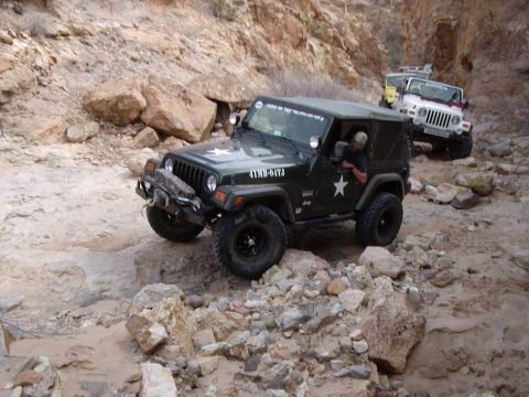 1996 Ford Bronco - Multiple Jeeps traverse a rocky canyon trail, with the lead vehicle displaying a star emblem.