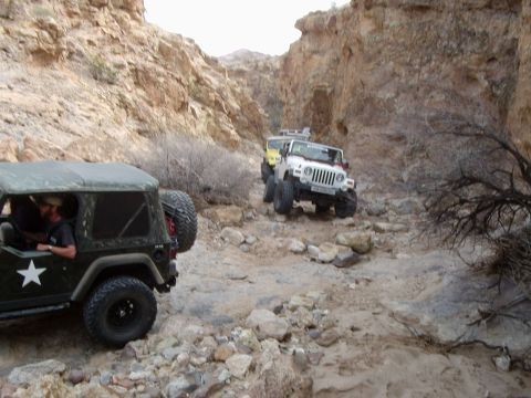 1996 Ford Bronco - Multiple Jeeps traverse a challenging off-road path through a narrow, rocky canyon.