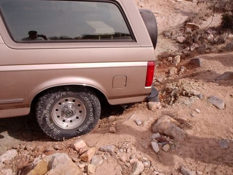 1996 Ford Bronco - The rear section of a tan Ford Bronco is visible on a rough, rocky terrain.
