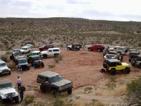 1996 Ford Bronco - A collection of off-road vehicles gathered in a dusty, arid landscape under a cloudy sky.