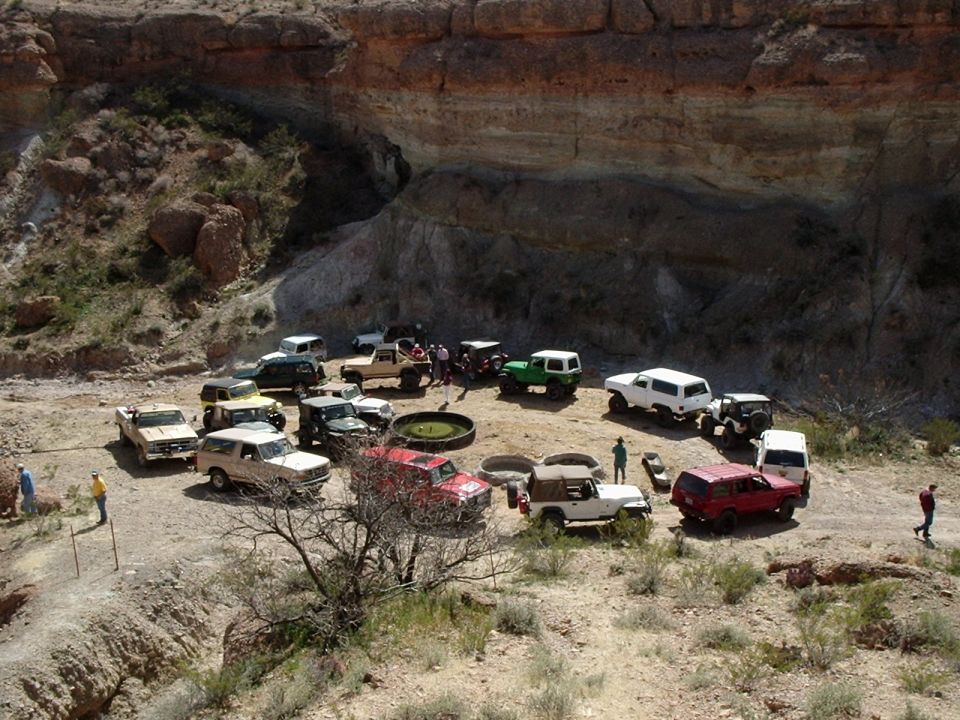 Group of off-road vehicles parked in a circle in a desert canyon with people standing around