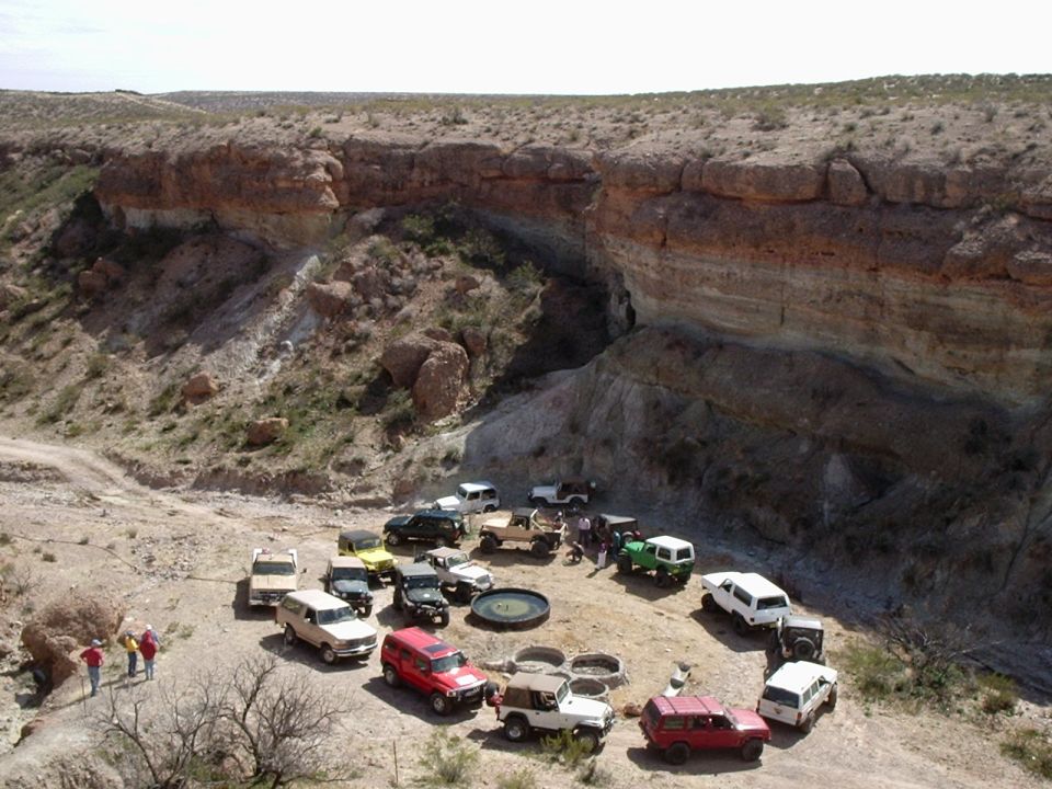 Off-road vehicles gathered in a dry, rocky canyon with layered cliffs