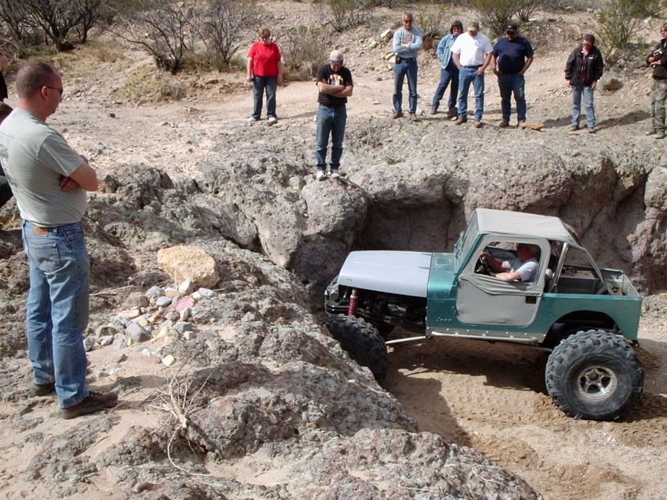 Green and silver off-road vehicle navigating a rocky trail with spectators