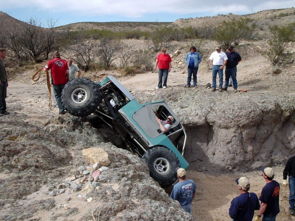 Teal off-road vehicle tilted precariously in a dirt ravine with large tires and exposed roll cage