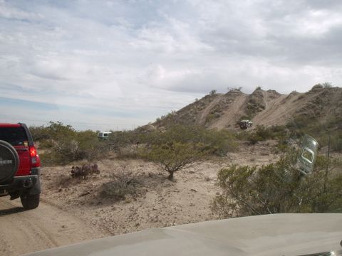 1996 Ford Bronco - Off-road vehicles navigate a dusty trail through a desert landscape with scrub brush and hills.