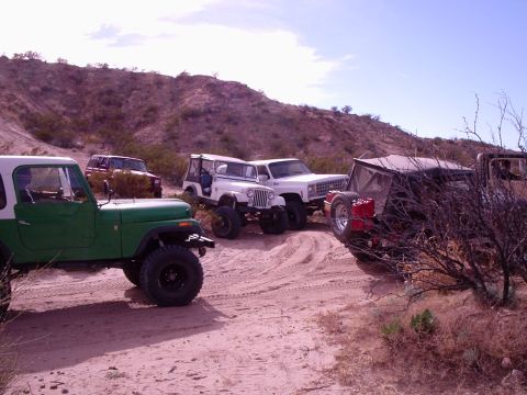 1996 Ford Bronco - A group of off-road vehicles are gathered on a sandy trail under a clear sky.