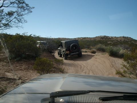 1996 Ford Bronco - Two Jeeps navigate a dusty, off-road trail through arid terrain under a clear blue sky.