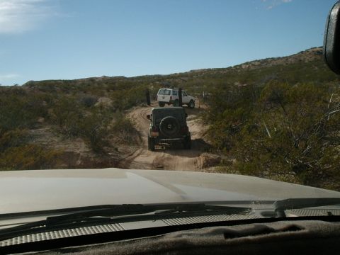 1996 Ford Bronco - Two SUVs navigate a dusty trail through a dry, brush-covered desert terrain under a clear blue sky.