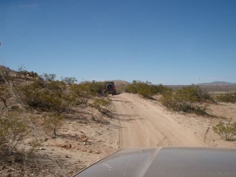 1996 Ford Bronco - A Jeep Wrangler navigates a dusty trail through a dry, arid environment under a clear blue sky.