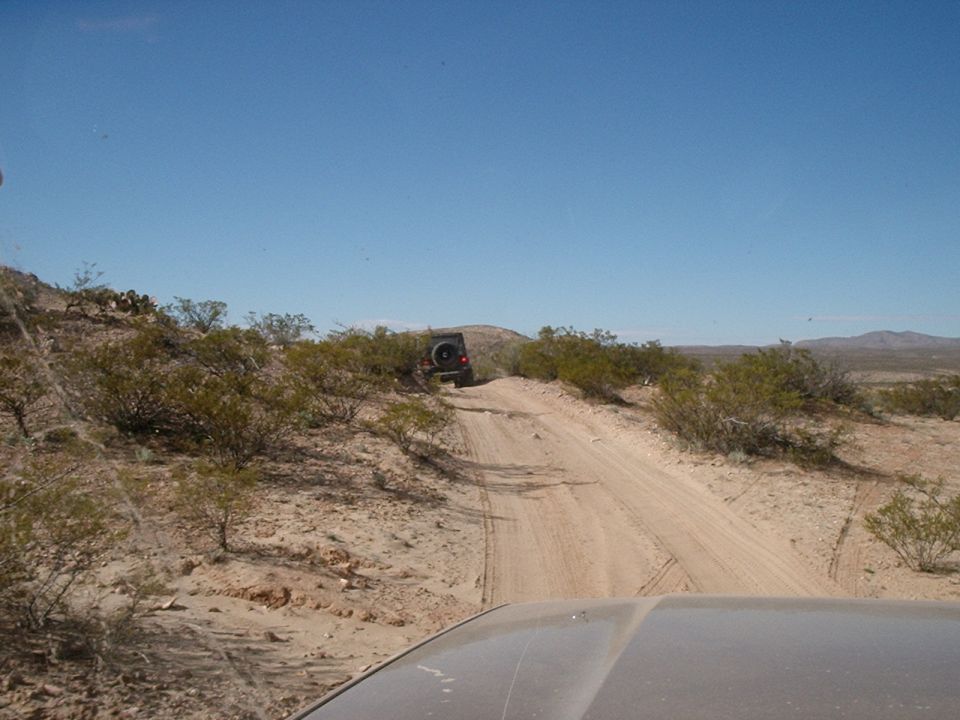 Dark colored Jeep Wrangler driving up a dirt trail in a desert landscape