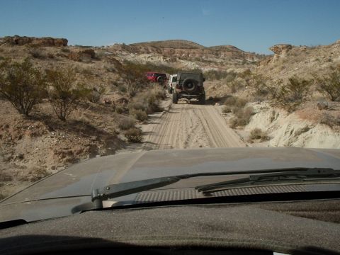 1996 Ford Bronco - A convoy of SUVs navigates a sandy track through a barren, rocky desert terrain under a clear blue sky.