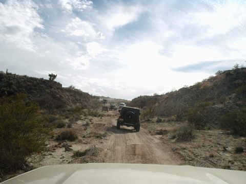 1996 Ford Bronco - A group of off-road vehicles navigates a dusty trail in a remote, arid environment.