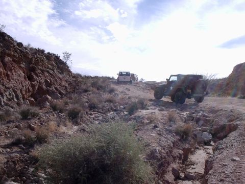 1996 Ford Bronco - Two off-road vehicles navigate a dusty, rocky trail under a cloudy sky.